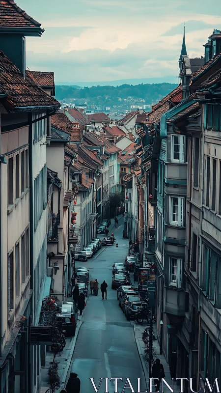 Narrow European street descends toward distant lakeside hills.