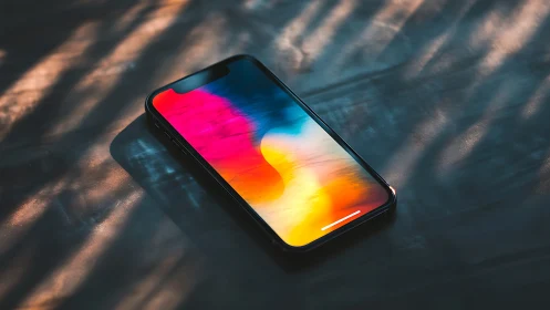 Black smartphone displaying vibrant gradient wallpaper under sunlight.