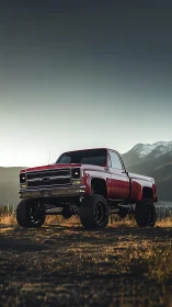 Lifted red classic pickup dominates moody alpine landscape.