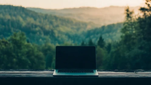 Laptop on rustic table overlooks tranquil misty forest valley