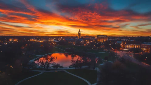 Fiery dusk skyline above city park lake and glowing campus.