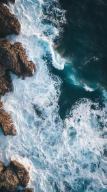 Aerial coastal surf collision with rugged rock formations.