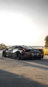 Low-slung black supercar on coastal road at golden hour.