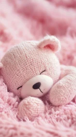 Soft pink knitted teddy bear resting on fluffy blanket.