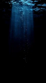 Vertical shaft of light and bubbles in dark underwater space.