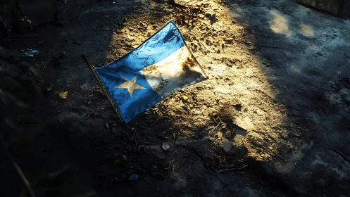 Tattered blue and white flag illuminated on debris-strewn ground