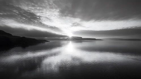 Monochrome coastal sunrise over calm reflective water.