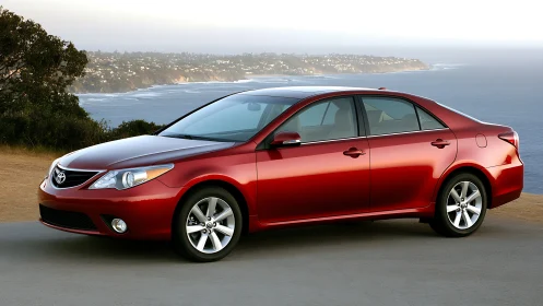 Red Toyota sedan parked beside coastal cliff road.