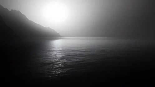 Monochrome coastal sunrise over calm reflective water surface.