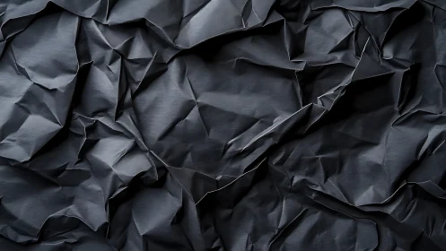 Dark crumpled paper surface forms sharp angular folds