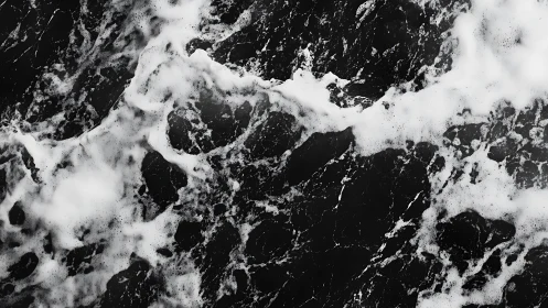 Monochrome aerial view of ocean surface with foam patterns.