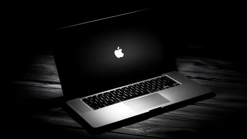 Apple laptop in low key light on wooden desk surface.