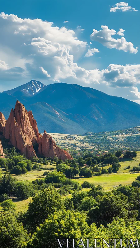 Red rock spires rise before forested mountains and clouds.