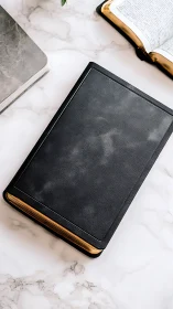 Black leather-bound book on marble desktop surface.