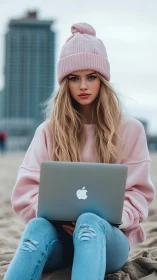 Young woman in pink sweater works on laptop at city beach