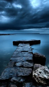 Stone jetty extends into calm blue sea under storm front