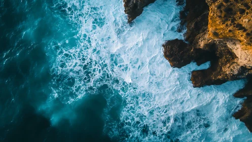 Turquoise waves greeting golden sea cliffs from above.