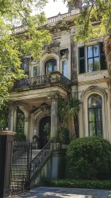 Weathered neoclassical mansion with wrought-iron veranda and palms.