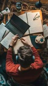 Student wearing headphones studies at cluttered wooden desk