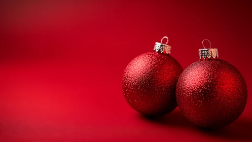 Three red glitter ornaments stand on uniform red surface