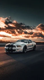 White muscle car on open highway under dramatic sunset sky.