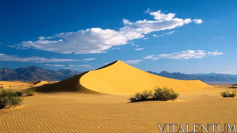 Golden desert dune under vivid blue sky with mountains.