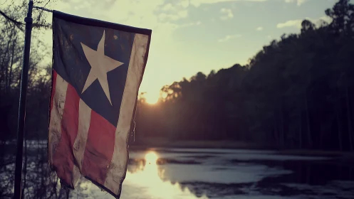 Weathered Lone Star flag at lakeside under soft sunset light.