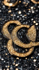 Golden glitter rings resting on sparkling black surface.
