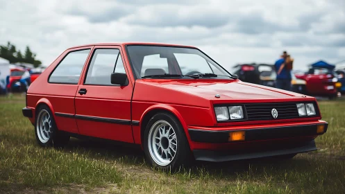 Lowered red VW hatchback with period-correct wheels on grass field