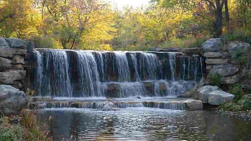 Serene woodland waterfall with stone cascade in autumn sunlight.