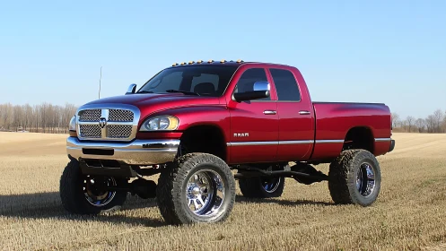 Lifted red pickup truck on rural harvested field landscape.