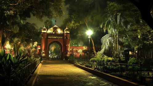 Illuminated park walkway leading to ornate gated archway.