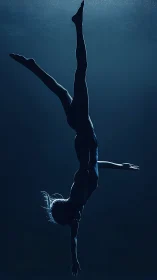 Underwater gymnast in inverted split pose in deep blue light.