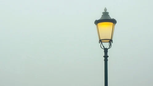 Solitary street lamp glows softly through dense morning fog.