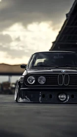 Stanced classic BMW front view under overcast industrial sky.