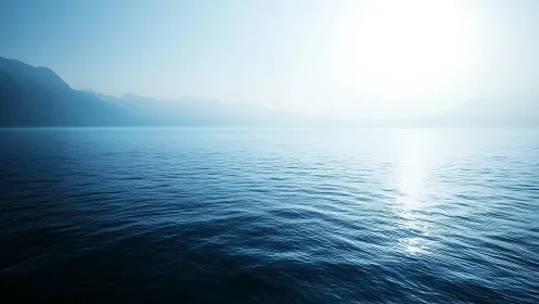 Calm blue sea under bright sun with distant hazy mountains.