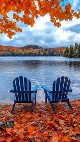 Blue Adirondack chairs overlook calm lake under peak autumn