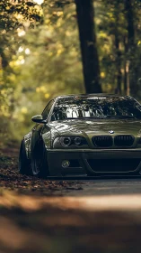 Slammed olive BMW sedan framed by forest bokeh light.