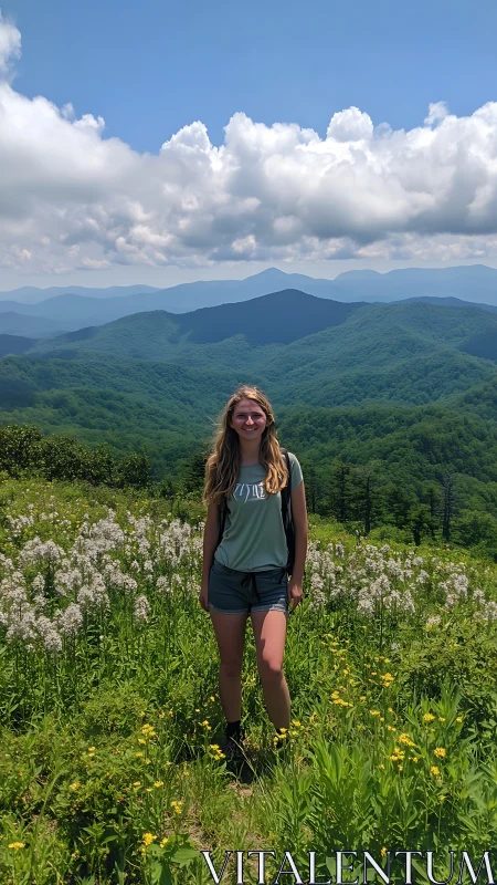 Hiker stands in sunlit wildflower meadow amid blue hazy peaks