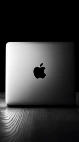 Backlit silver laptop on wooden desk against deep black void