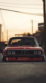 Vintage red BMW front profile in golden-hour street scene.