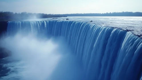 Wide misty waterfall edge under soft blue daylight.