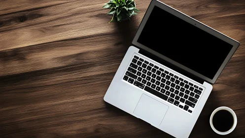 Overhead view of aluminum laptop on wood desk with coffee and plant