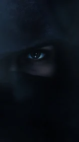 Shrouded eye in shadowed hood with cinematic low key lighting.