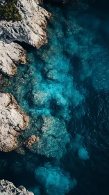 Rocky coast meets clear turquoise sea in vertical aerial view