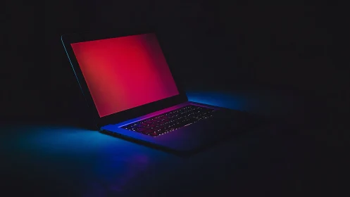 Open laptop glows with neon red and blue light in darkness