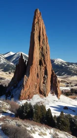 Tall red sandstone spire stands in snowy mountain landscape