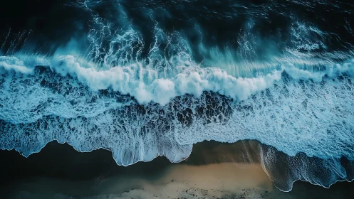 Aerial ocean surf crashing over dark sand shoreline.