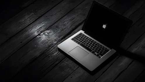 Sleek laptop on dark wooden boards in dramatic spotlight.