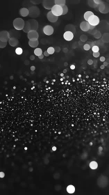 Monochrome bokeh lights over dark glitter surface.